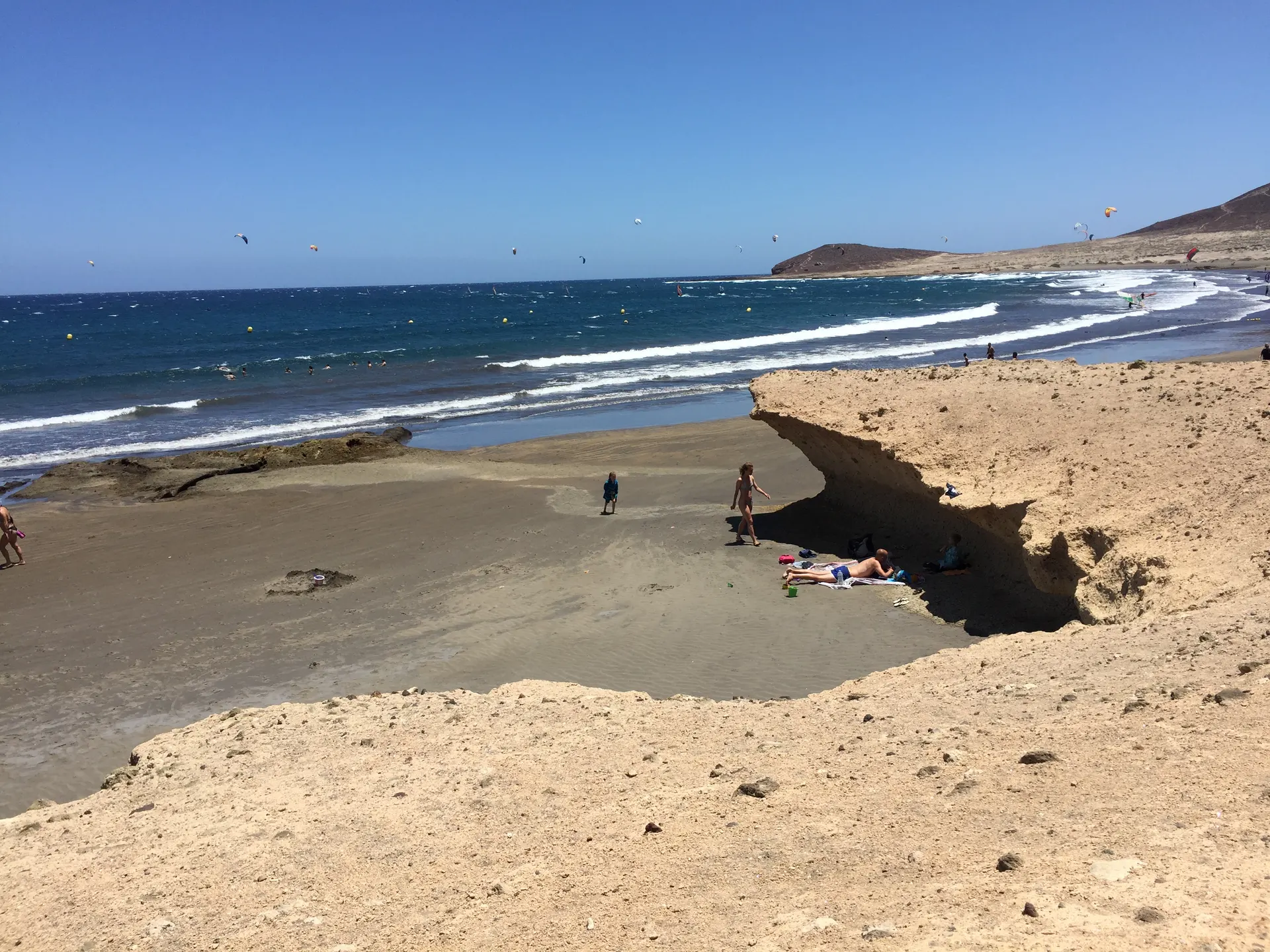 Strand von El Médano mit Badenden, Kitesurfern und Montaña Roja im Hintergrund.